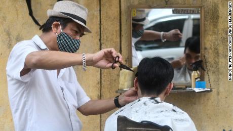 A roadside barber wearing a face mask makes a haircut to a client in Hanoi.