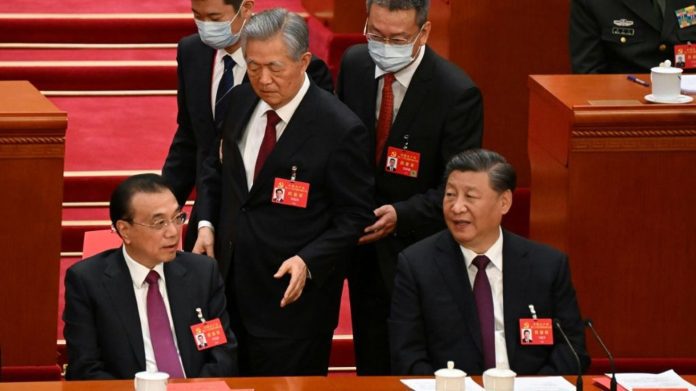 L'ex-président chinois Hu Jintao (c), entre le chef de l'Etat actuel Xi Jinping (d) et le Premier ministre Li Keqiang (g), est emmené vers la sortie lors de la cérémonie de clôture du congrès du Parti communiste, à Pékin le 22 octobre 2022